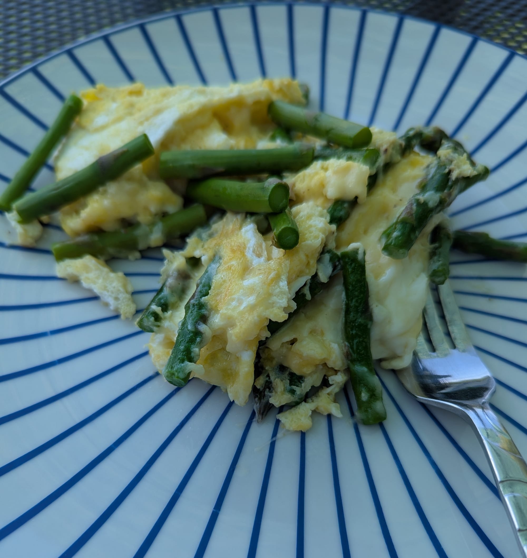 A misshapen omelet with asparagus on a plate with a fork sitting nearby