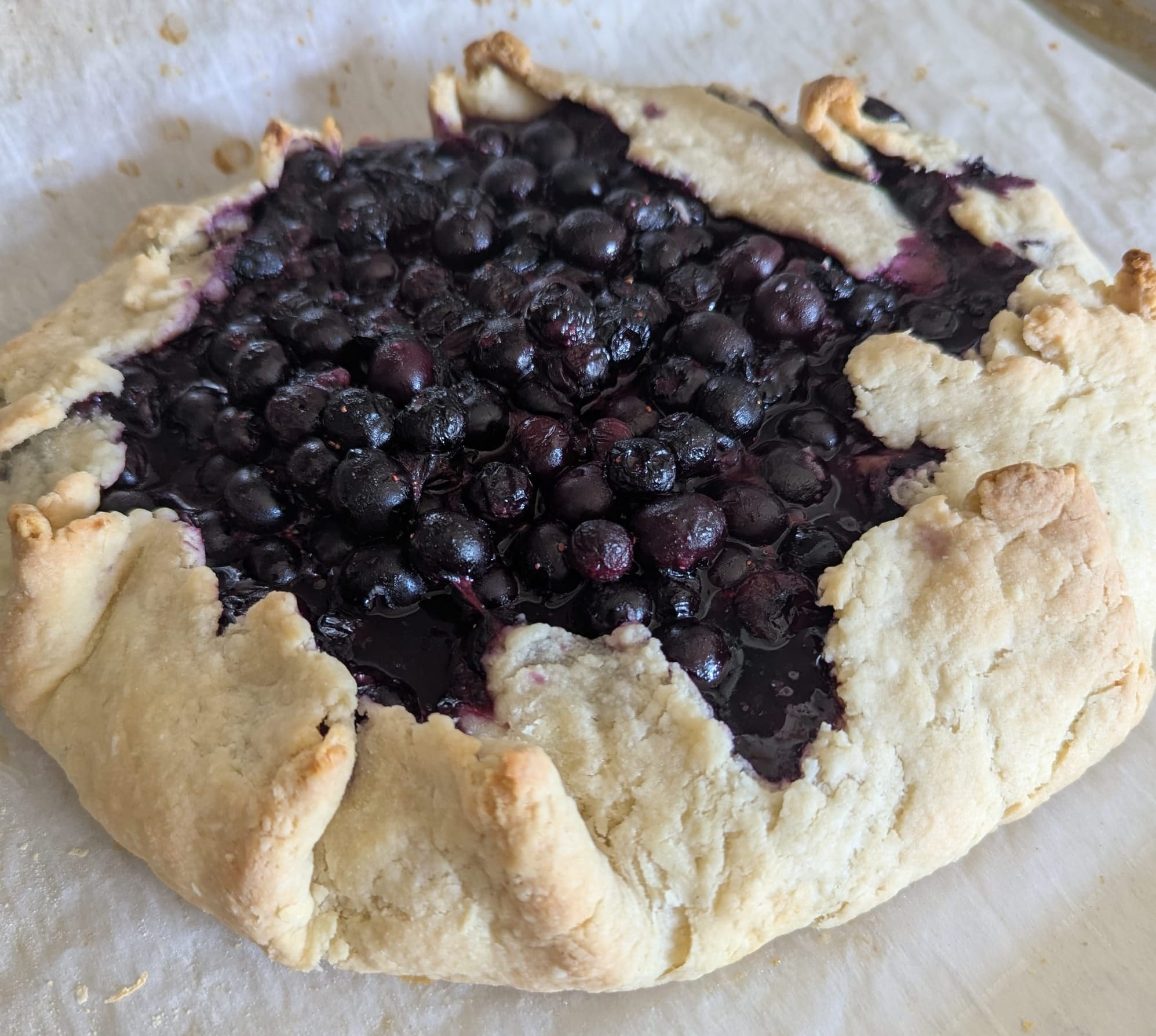 Close-up photo of jammy blueberries folded inside a flaky crust, like an open-faced pie