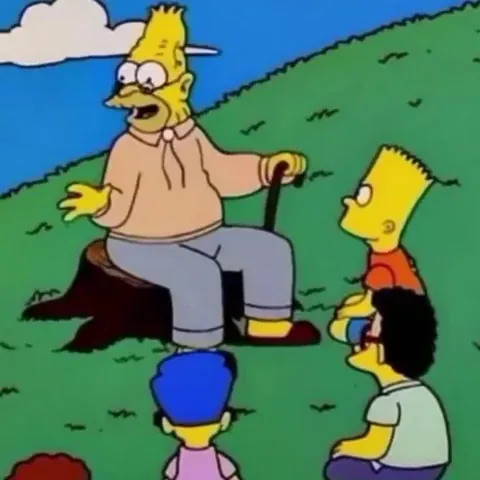 Still image of Grandpa Simpson sitting on a log and telling a story to Bart, Milhouse, and other kids sitting around him