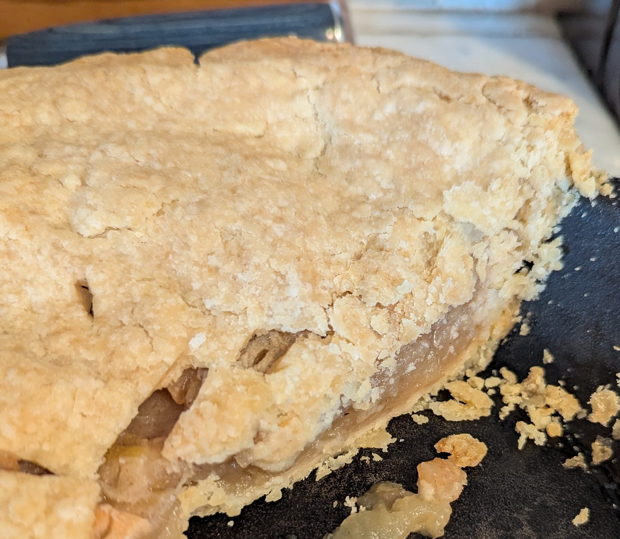 Close-up photo of an apple pie with a flaky, golden crust, showing a cross section of apple filling