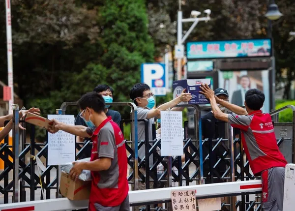 Des livreurs remettent des colis par-dessus une clôture à des résidents dans l'arrondissement de Xicheng à Beijing, capitale